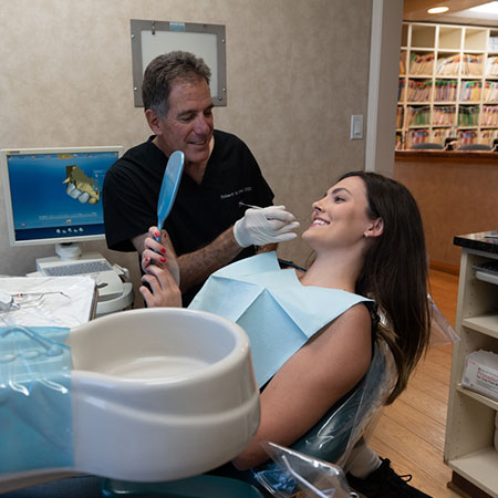 Dr. Robert checking the teeth of a young woman who is smiling in the dentist's chair